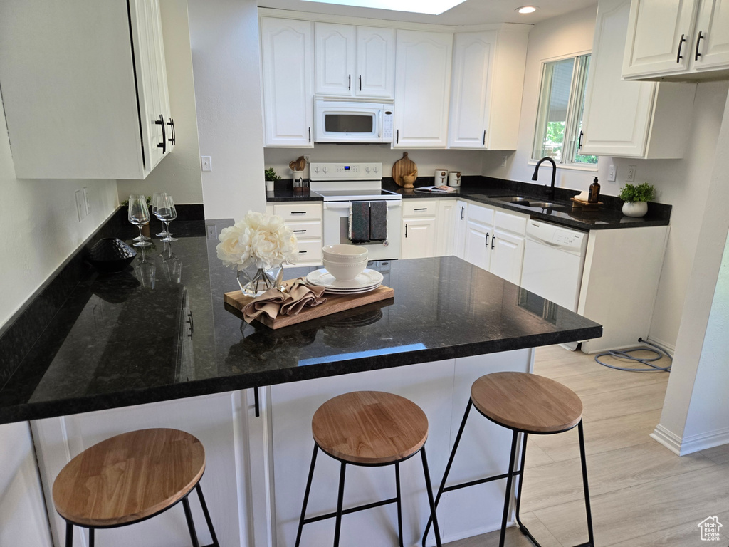 Kitchen featuring white appliances, a sink, a peninsula, a kitchen bar, and white cabinetry