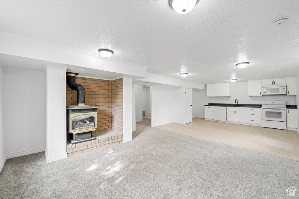Unfurnished living room featuring a textured ceiling, light colored carpet, a wood stove, baseboards, and a sink