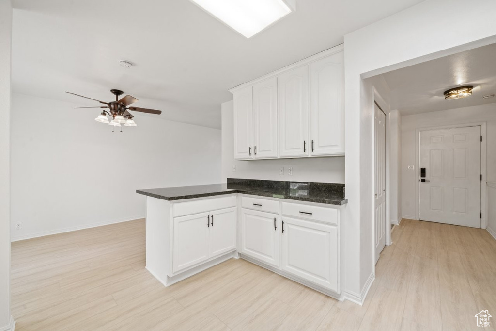 Kitchen with a peninsula, white cabinets, light wood finished floors, ceiling fan, and baseboards