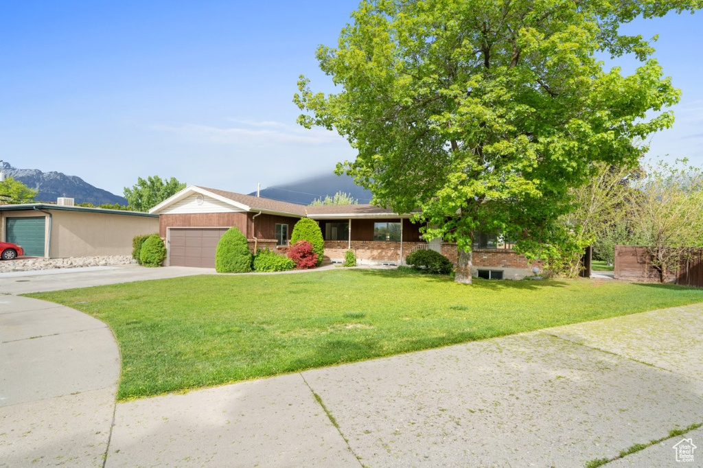 Ranch-style house featuring driveway, a front yard, an attached garage, and a mountain view
