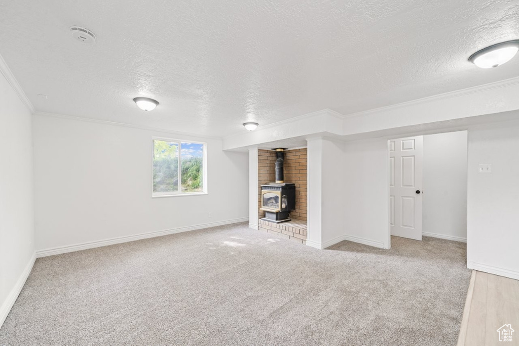 Unfurnished living room featuring a wood stove, a textured ceiling, carpet, ornamental molding, and baseboards