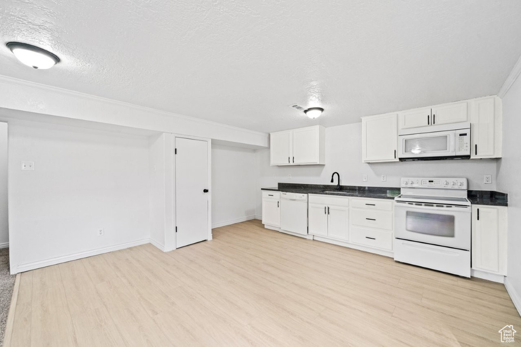 Kitchen with white appliances, light wood-type flooring, dark countertops, white cabinetry, and baseboards