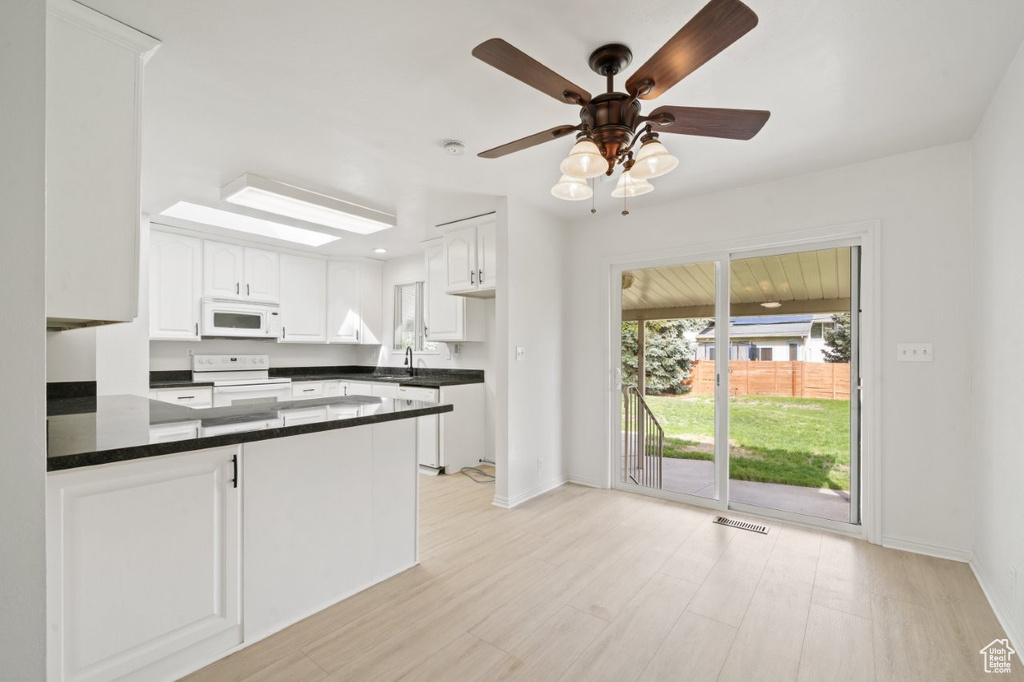 Kitchen featuring white appliances, dark countertops, white cabinetry, and a peninsula