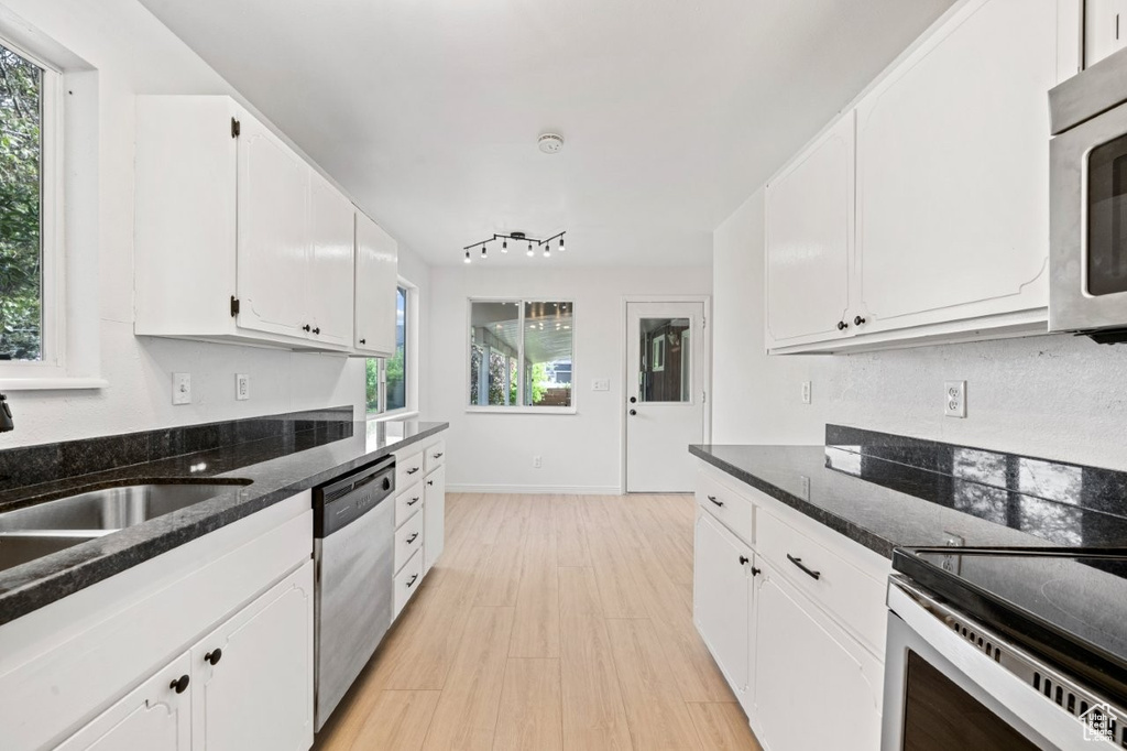 Kitchen featuring appliances with stainless steel finishes, healthy amount of natural light, white cabinetry, and light wood-style floors