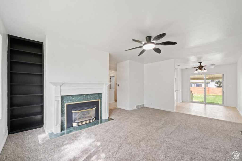 Unfurnished living room with a ceiling fan, carpet, a fireplace, baseboards, and built in shelves