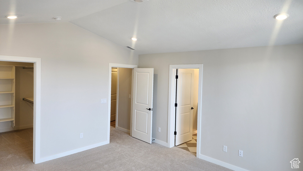Unfurnished bedroom featuring light colored carpet, a spacious closet, lofted ceiling, baseboards, and recessed lighting