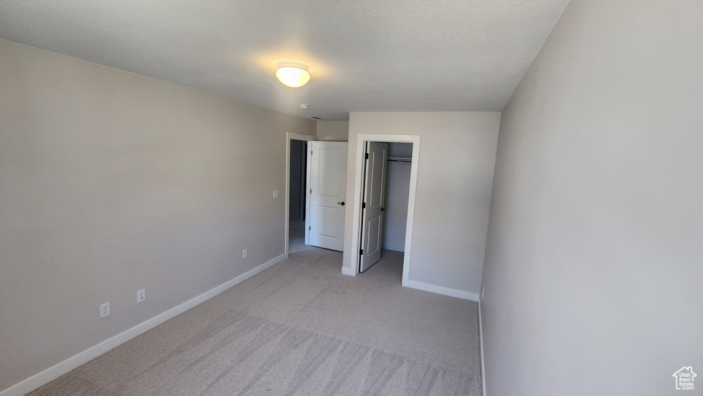 Unfurnished bedroom featuring light colored carpet, baseboards, a closet, and a spacious closet