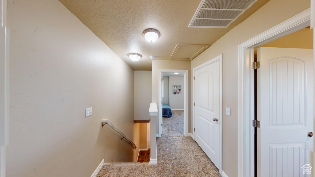 Hall featuring an upstairs landing, carpet, baseboards, and a textured ceiling