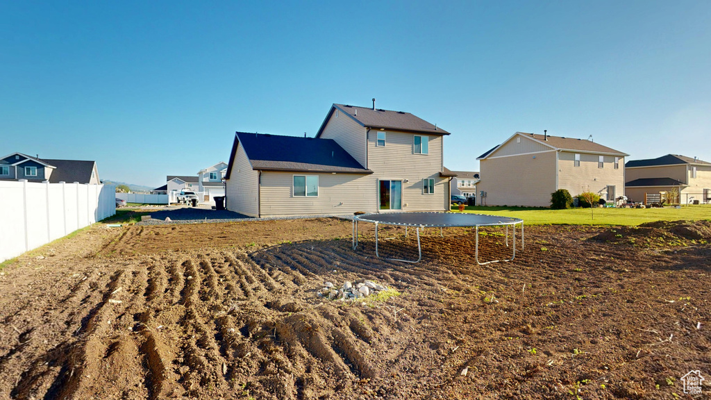 Rear view of house with a trampoline, fence, and a residential view