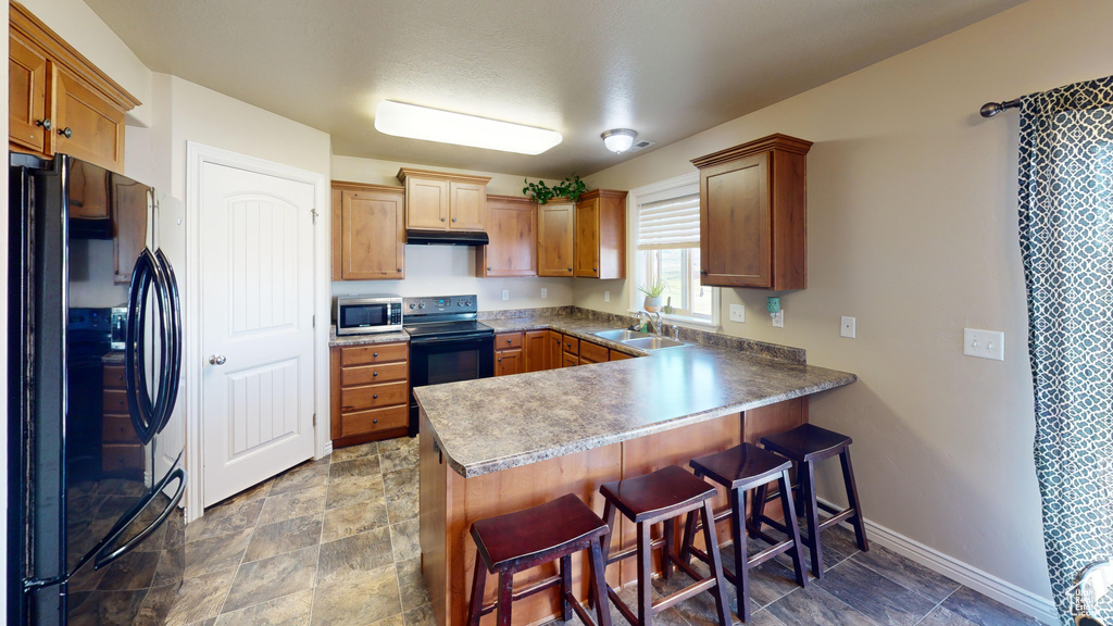 Kitchen featuring black appliances, a peninsula, under cabinet range hood, a sink, and a kitchen bar