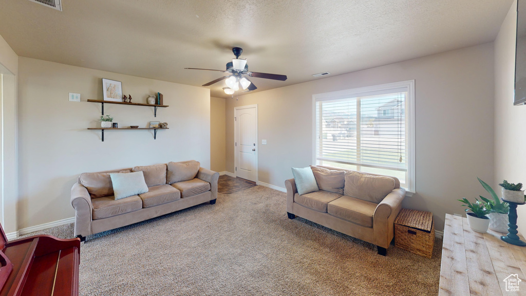 Carpeted living area featuring ceiling fan and baseboards