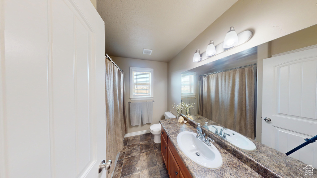 Bathroom featuring vanity, baseboards, toilet, stone finish flooring, and a shower with shower curtain