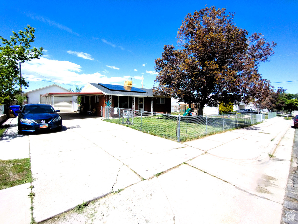 Single story home with concrete driveway, roof mounted solar panels, and a carport