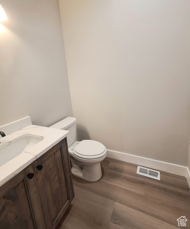 Half bath featuring vanity, wood finished floors, toilet, and baseboards