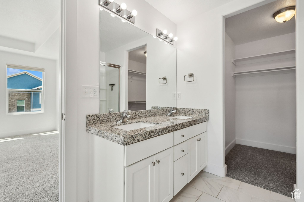 Bathroom with a spacious closet, double vanity, baseboards, and a shower with shower door