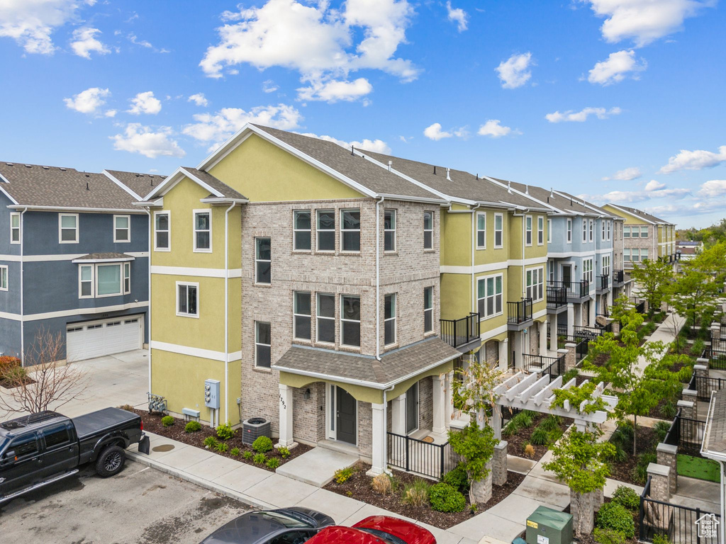 View of property featuring a residential view, an attached garage, central air condition unit, and uncovered parking