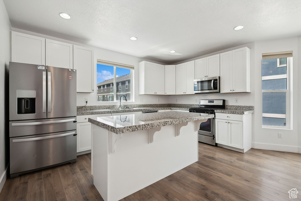 Kitchen with stainless steel appliances, white cabinets, a center island, a sink, and a breakfast bar area