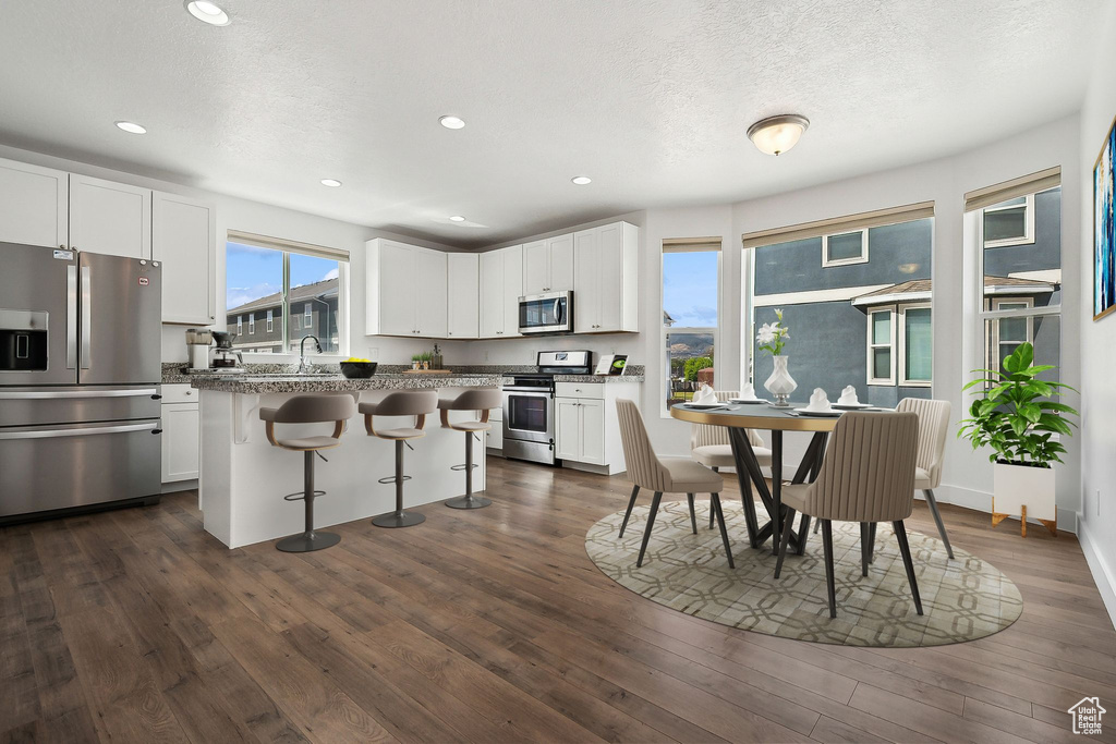 Kitchen featuring stainless steel appliances, a breakfast bar, white cabinets, dark wood-style floors, and recessed lighting