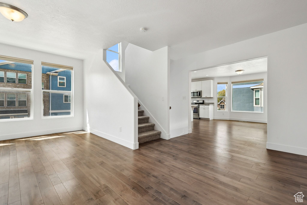 Unfurnished living room with baseboards, stairs, and dark wood-style flooring