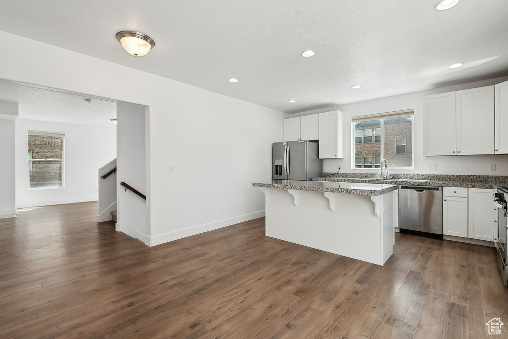 Kitchen with appliances with stainless steel finishes, a breakfast bar area, a center island, white cabinets, and stone counters