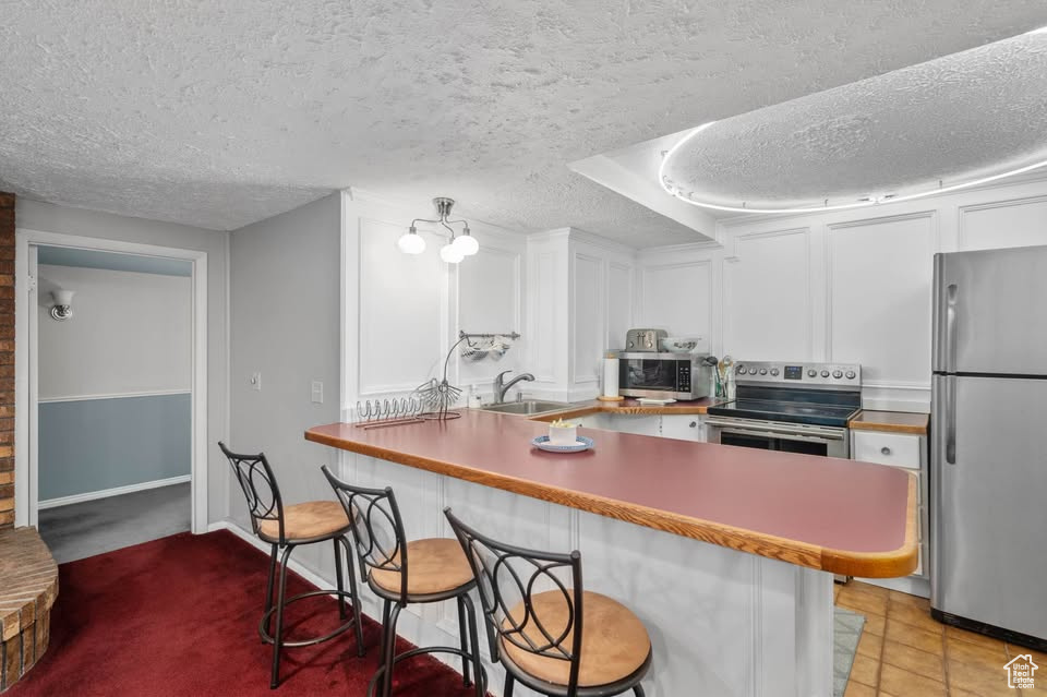 Kitchen featuring appliances with stainless steel finishes, a textured ceiling, a kitchen bar, white cabinets, and a peninsula