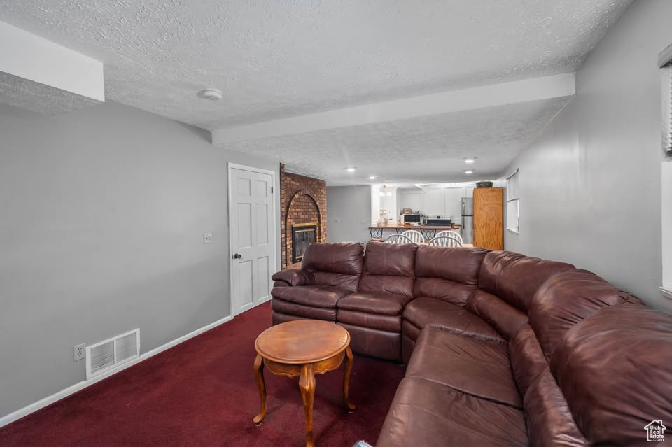 Living area featuring a textured ceiling, carpet flooring, a brick fireplace, and baseboards