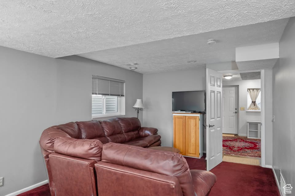 Living room featuring dark colored carpet, a textured ceiling, and baseboards