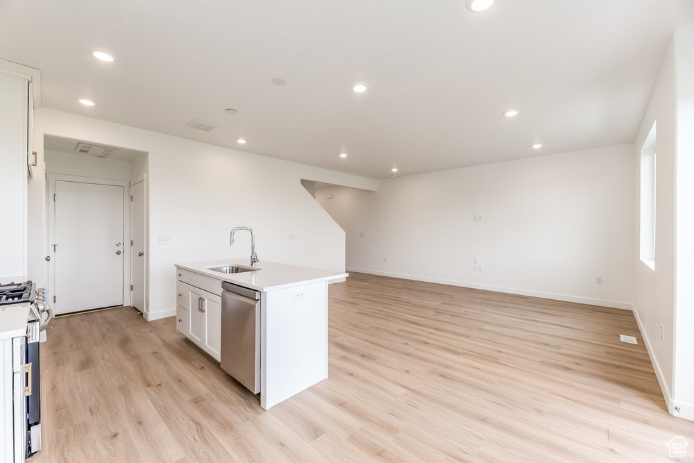 Kitchen with a sink, appliances with stainless steel finishes, light wood-type flooring, light countertops, and an island with sink