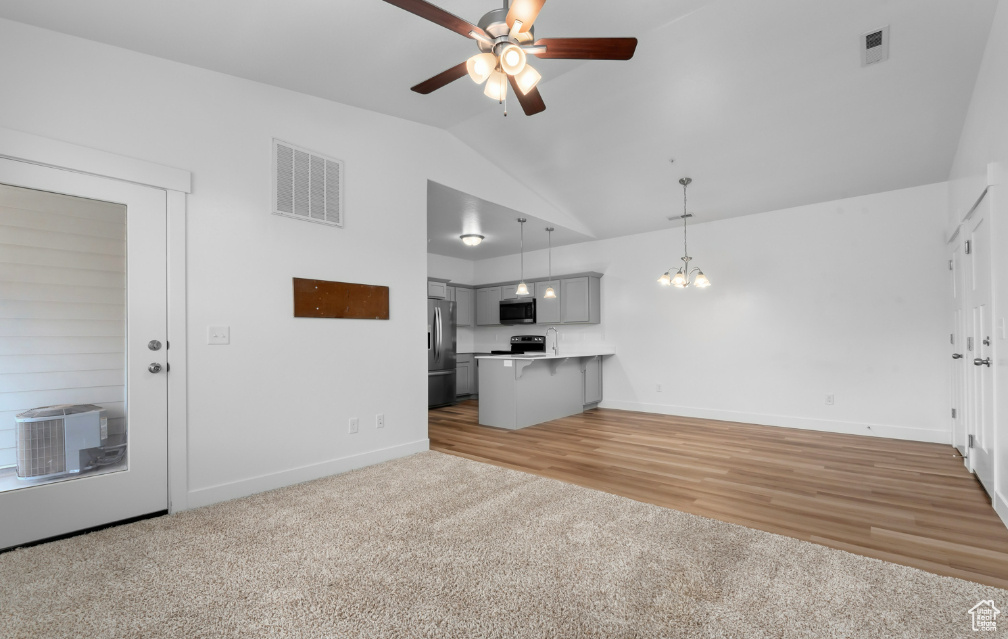 Unfurnished living room with ceiling fan, vaulted ceiling, baseboards, a chandelier, and light colored carpet