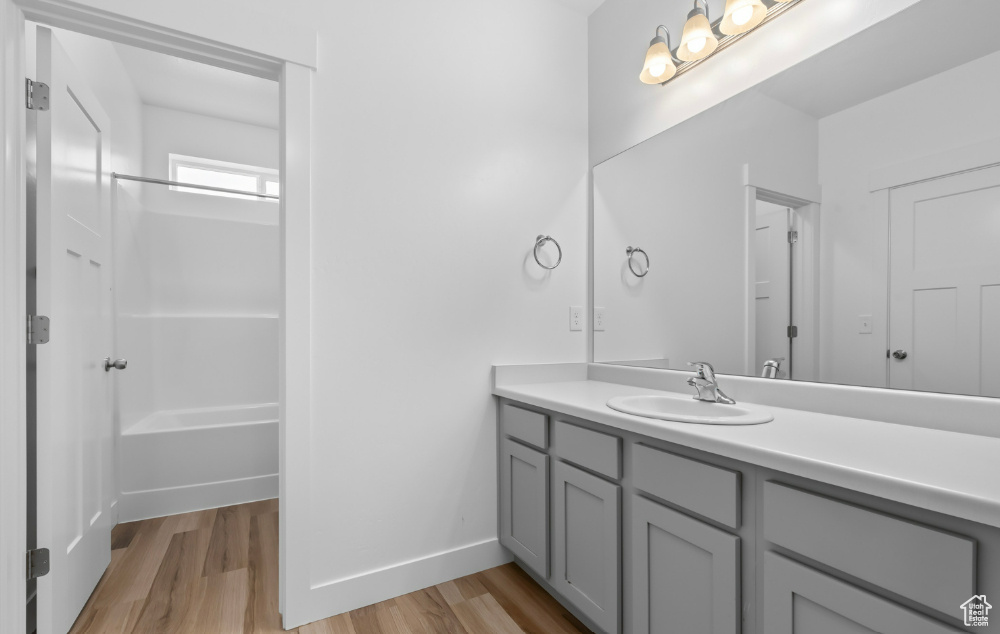 Bathroom featuring wood finished floors, vanity, shower / bathtub combination, and baseboards