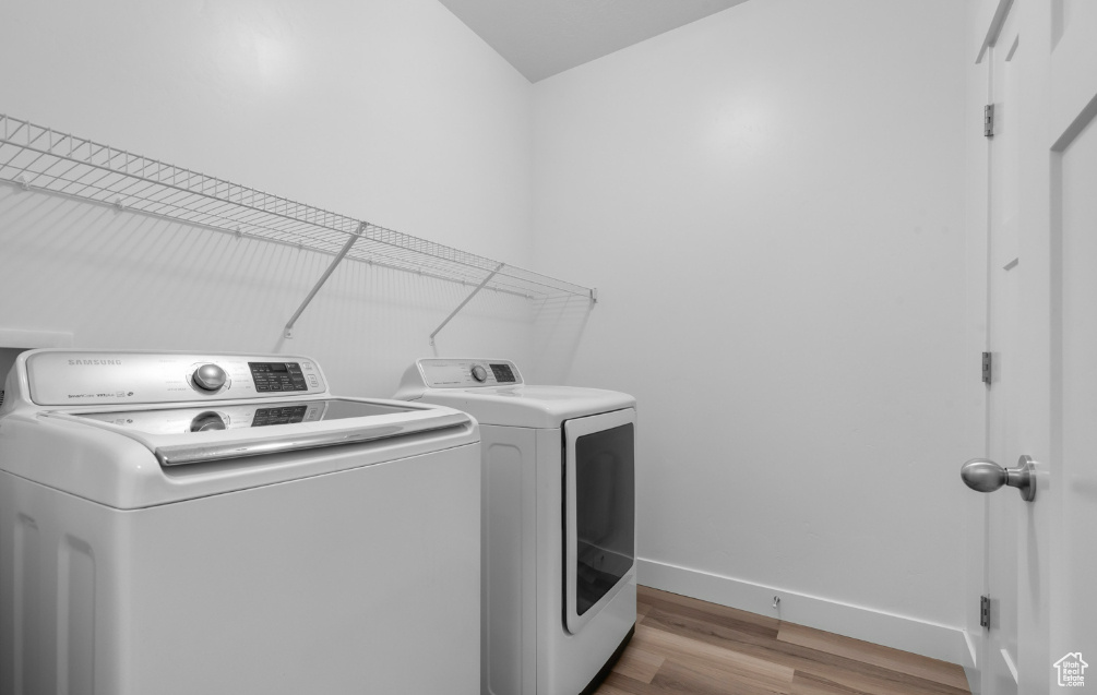 Laundry room with washing machine and dryer, wood finished floors, and baseboards