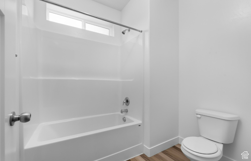 Full bathroom with baseboards, wood finished floors, toilet, and shower / tub combination