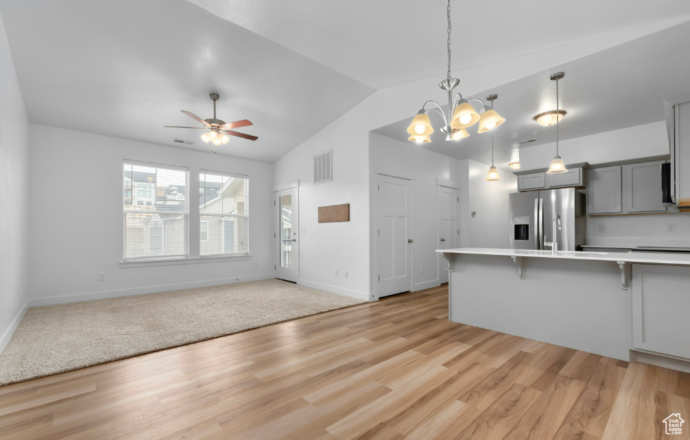 Kitchen with stainless steel fridge, gray cabinets, a kitchen breakfast bar, light countertops, and lofted ceiling