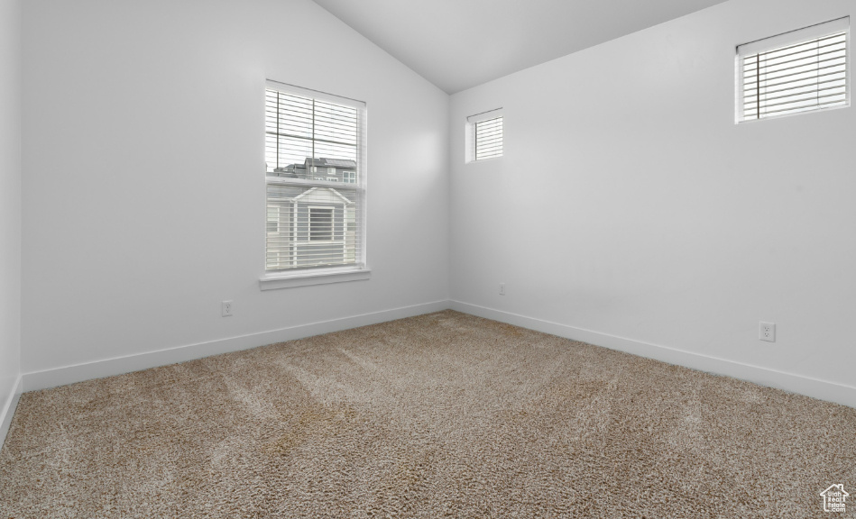 Carpeted empty room featuring lofted ceiling and baseboards