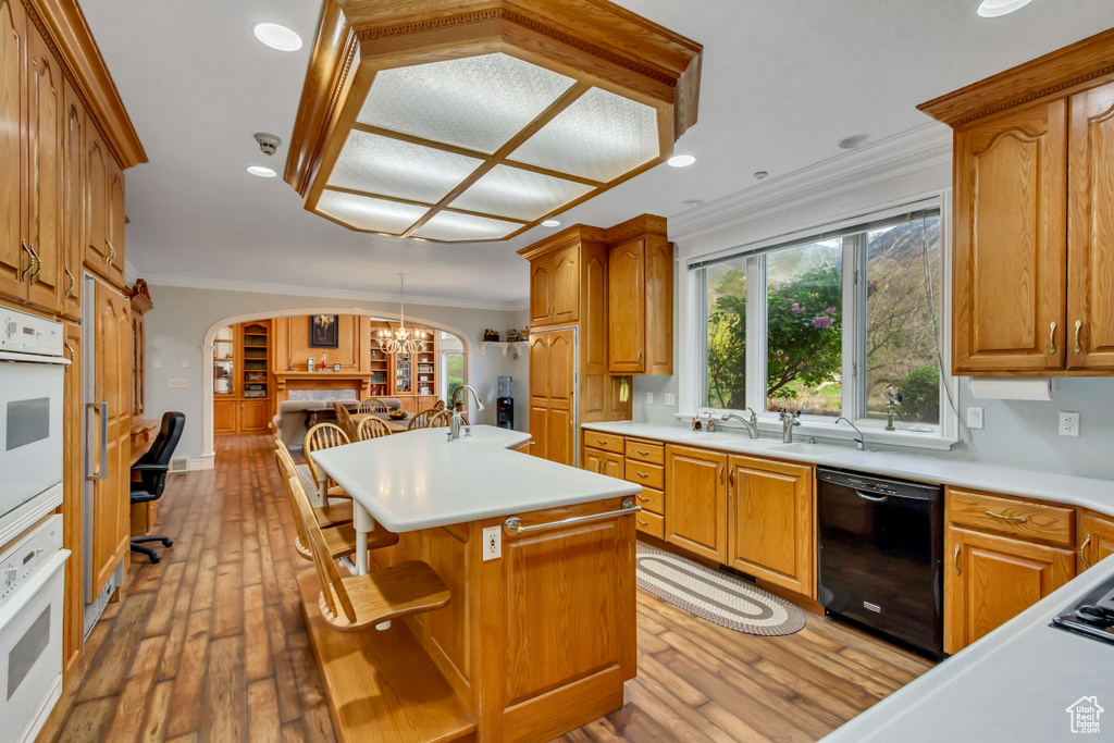 Kitchen featuring dishwasher, crown molding, arched walkways, light countertops, and light wood-style floors