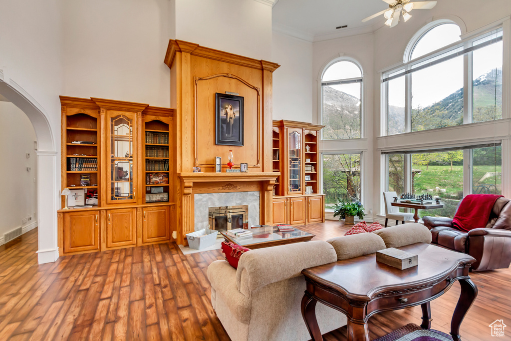 Living area featuring a towering ceiling, a premium fireplace, arched walkways, ceiling fan, and hardwood / wood-style flooring