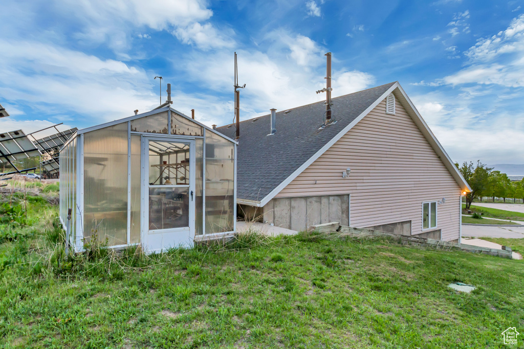 Rear view of house featuring a greenhouse, roof with shingles, an outdoor structure, and a lawn