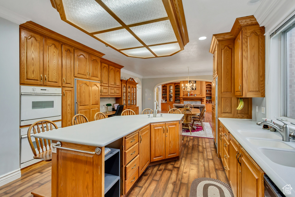 Kitchen featuring white oven, a kitchen island with sink, arched walkways, wood-type flooring, and light countertops