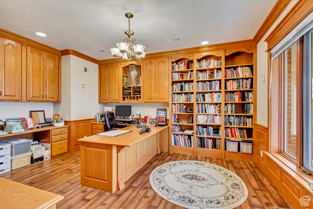 Office area featuring light wood finished floors, ornamental molding, built in study area, wainscoting, and a chandelier