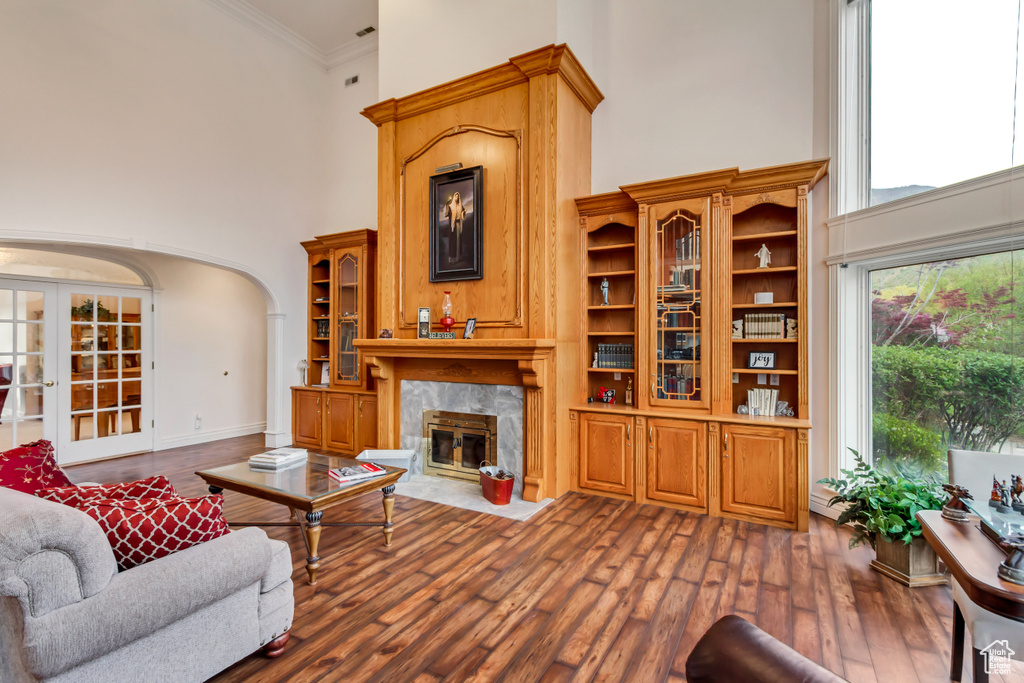 Living area featuring a high ceiling, arched walkways, a fireplace, dark wood-style flooring, and crown molding