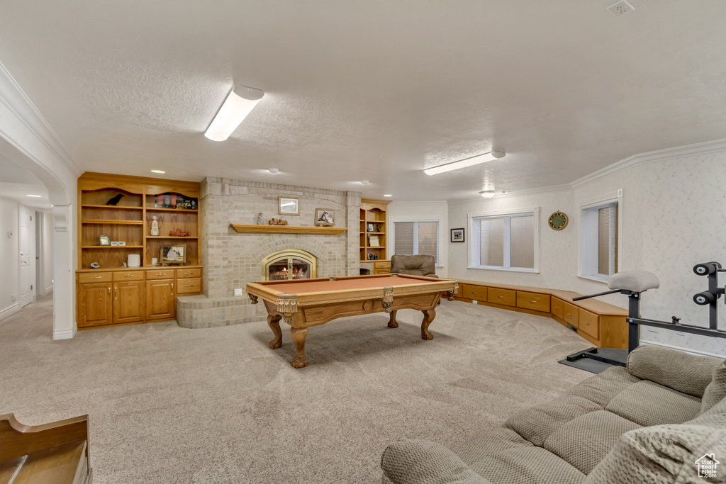 Game room featuring light colored carpet, a brick fireplace, crown molding, built in shelves, and a textured ceiling