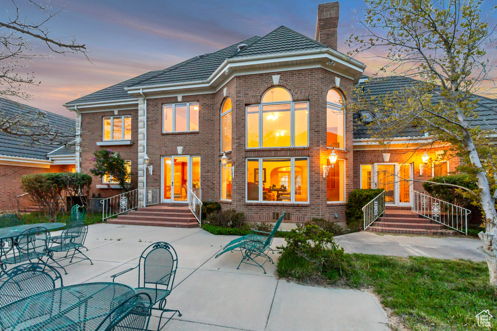 Back of property featuring a chimney, brick siding, a patio, and a tile roof