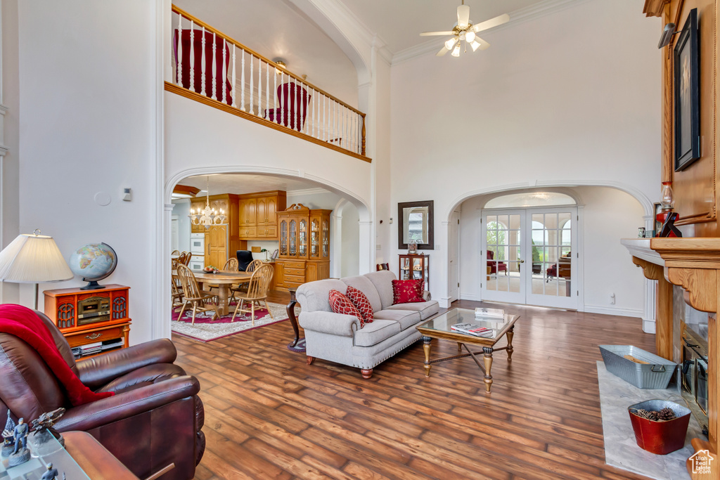 Living room with arched walkways, ceiling fan, ornamental molding, hardwood / wood-style floors, and a towering ceiling