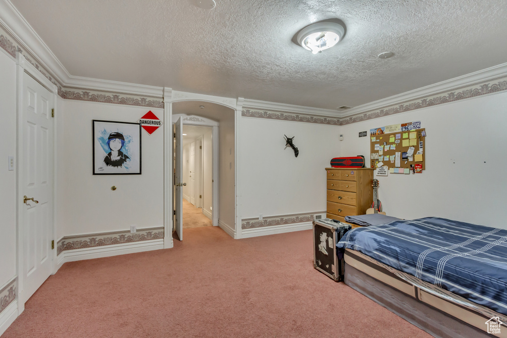 Bedroom with a textured ceiling, light colored carpet, ornamental molding, arched walkways, and baseboards