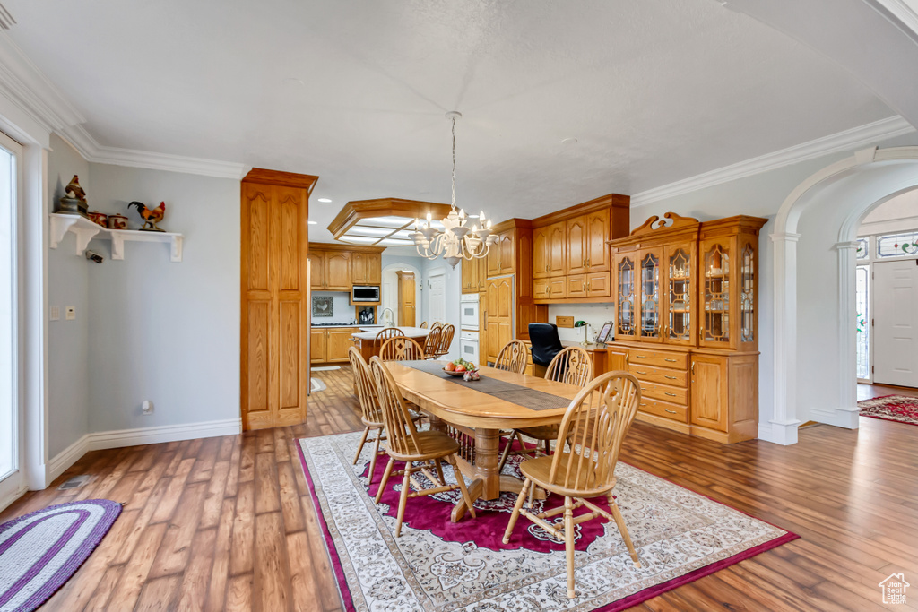 Dining space featuring arched walkways, light wood-type flooring, a chandelier, crown molding, and baseboards