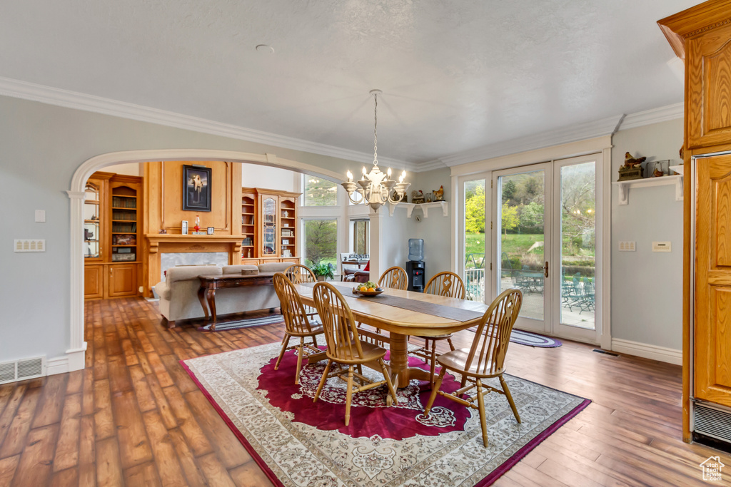 Dining room featuring a chandelier, ornamental molding, arched walkways, wood-type flooring, and baseboards
