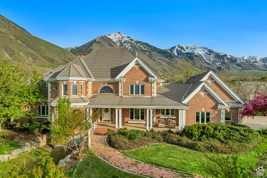 View of front of home featuring a tile roof, brick siding, a porch, and a mountain view