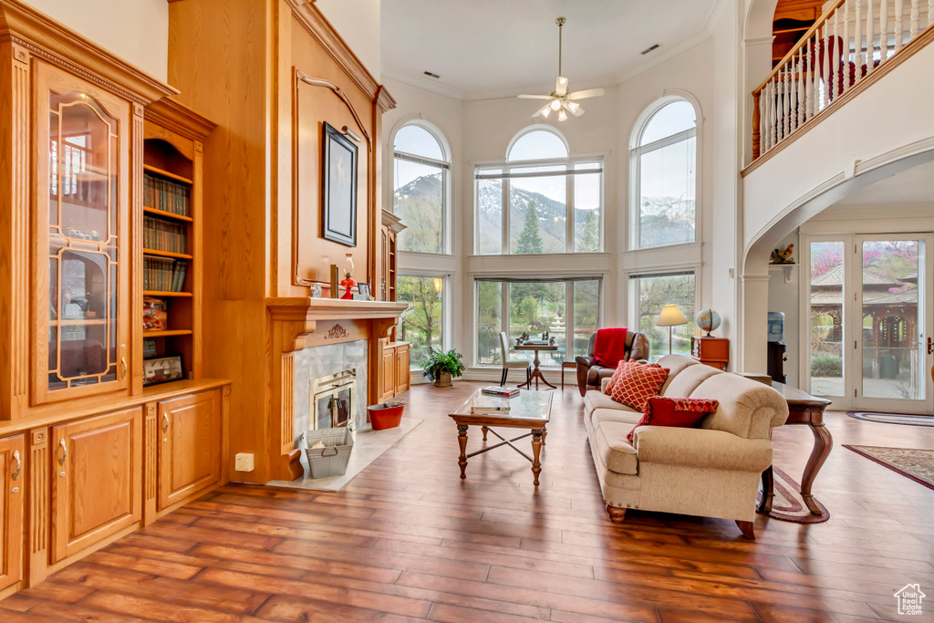 Living area with ceiling fan, a towering ceiling, a tiled fireplace, crown molding, and arched walkways