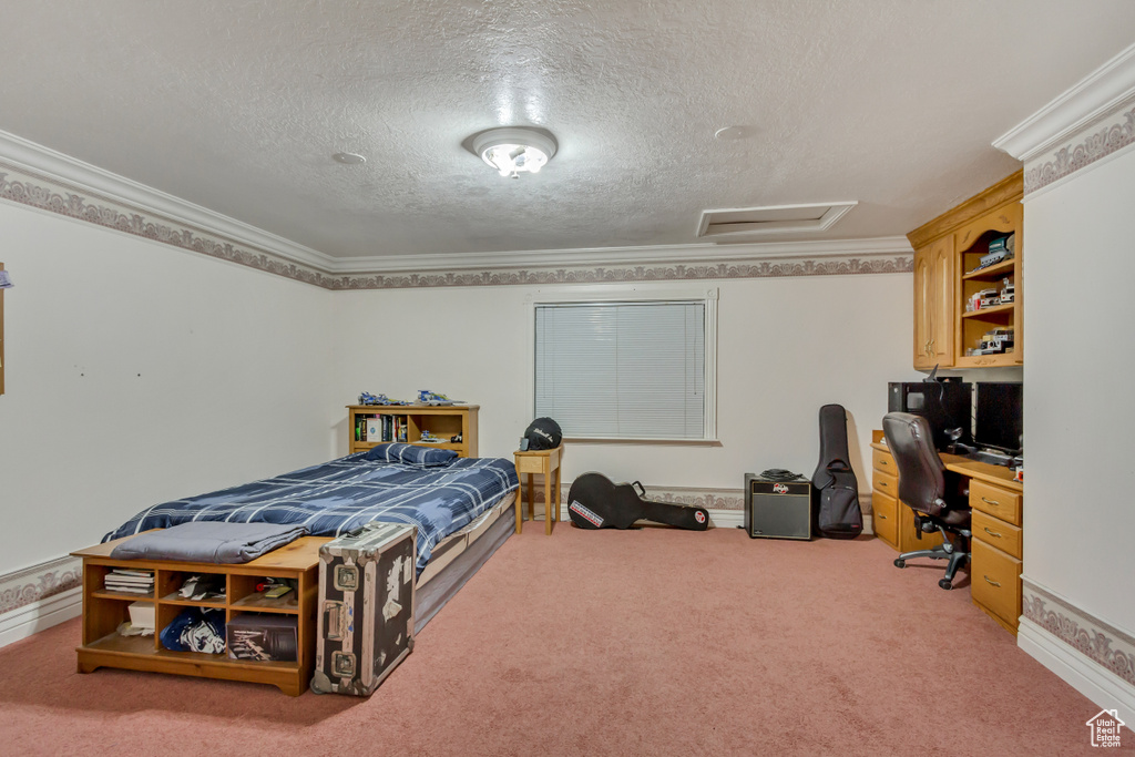 Bedroom featuring an office area, a textured ceiling, attic access, carpet floors, and ornamental molding