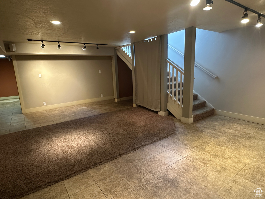 Basement with rail lighting, stairs, baseboards, and tile patterned flooring